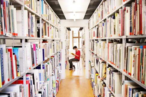 lesende Frau sitzt zwischen zwei deckenhohen Bücherregalen