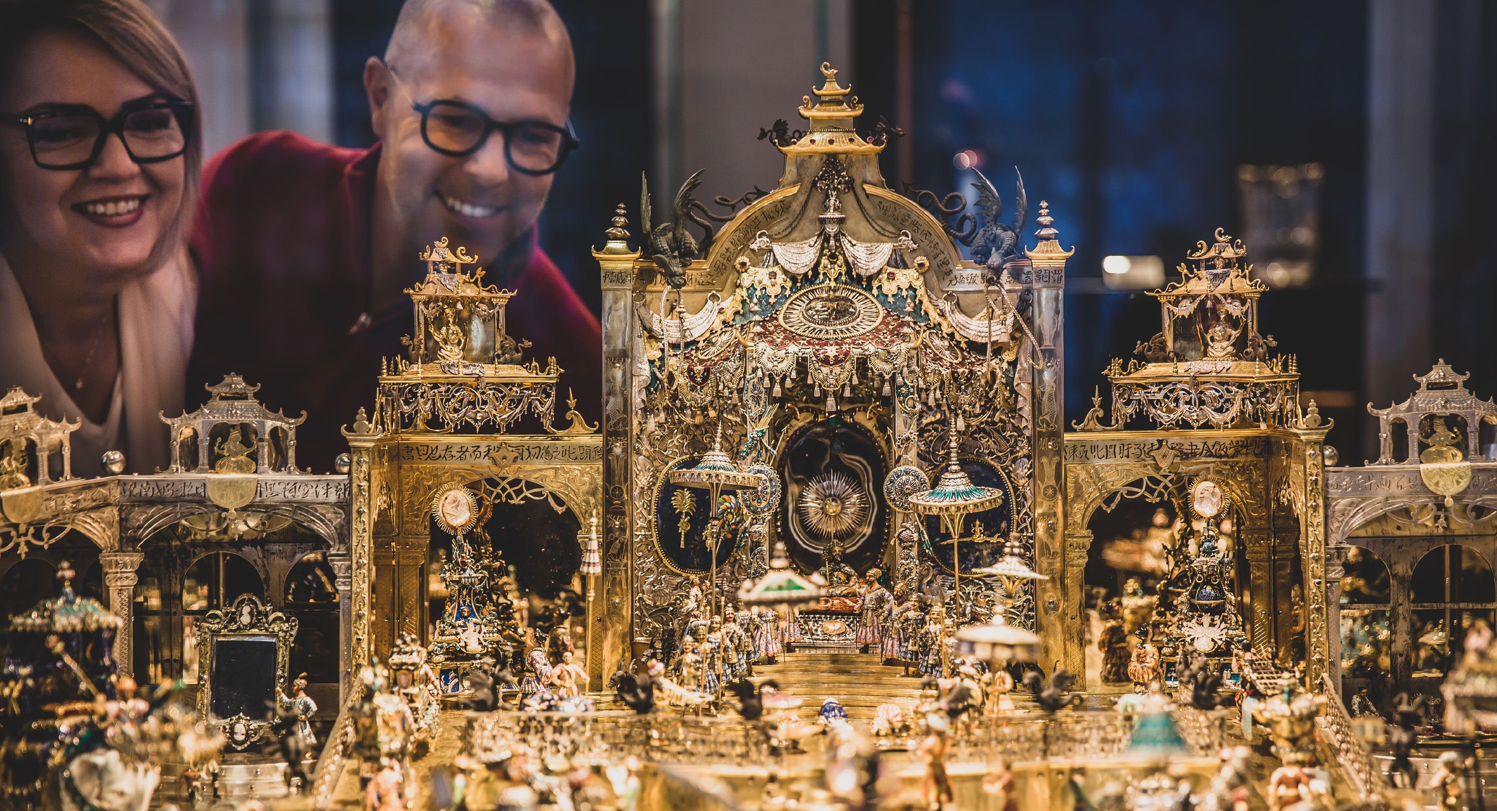 zwei Personen schauen auf eine goldene Miniaturszenerie