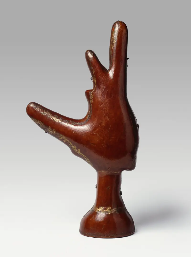 Zu sehen ist ein lederbezogenes Etui, das in seiner Form einer Hand ähnelt und als Transporthülle der Pretiose einer Prunkkanne in Schiffsform fungierte und das kürfürstlich-königliche Haus auf seinen Reisen an den Königshof nach Warschau begleitete.