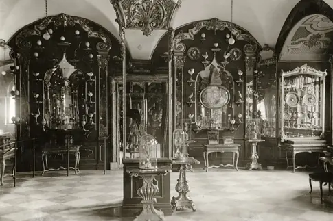 Auf diesem historischen Foto ist die Raumausstattung des Emailzimmers von 1930 zu sehen. Der Mittelpfeiler ist verspiegelt. Die Wände sind mit Holzpanelen, Spiegeln und zahlreichen Kunstobjekten bestückt.