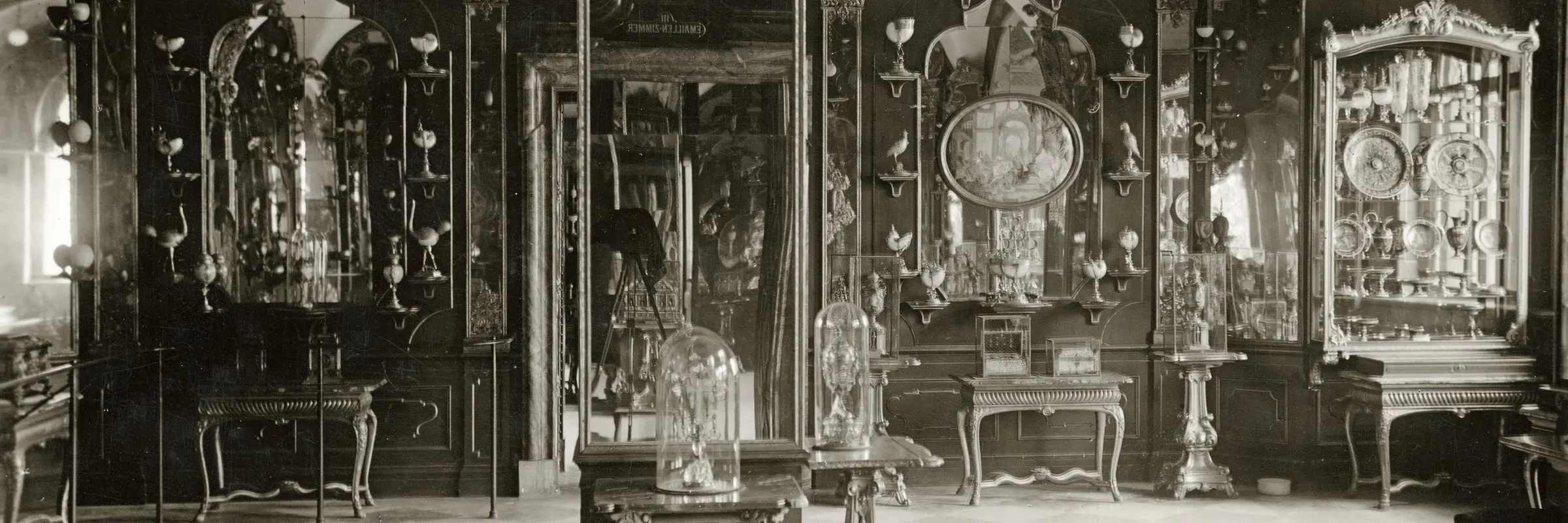 Auf diesem historischen Foto ist die Raumausstattung des Emailzimmers von 1930 zu sehen. Der Mittelpfeiler ist verspiegelt. Die Wände sind mit Holzpanelen, Spiegeln und zahlreichen Kunstobjekten bestückt.