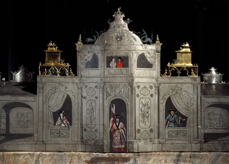 Die Abbildung zeigt die Rückseite des Hofstaats zu Dehli. Darauf sind zahlreiche Figuren in asiatisch anmutender Kleidung zu sehen.