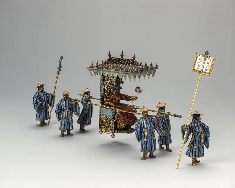 Die Abbildung zeigt eine 6köpfige Figurengruppe in asiatisch anmutender Kleidung. Vier von Ihnen tragen eine Sänfte. Darin befindet sich ebenfalls eine Figur.